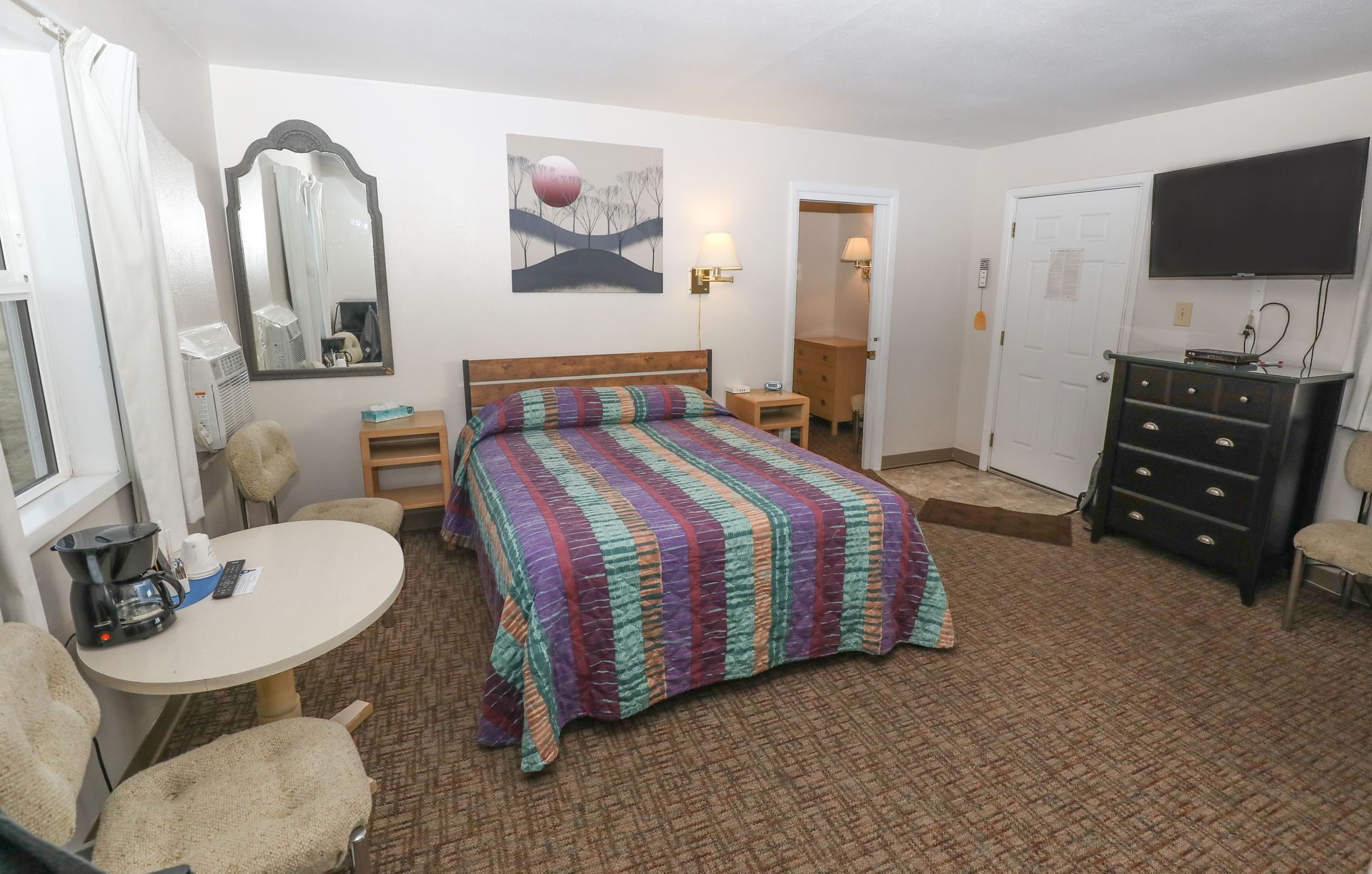 A hotel room with a bed , table , chairs , dresser and television.