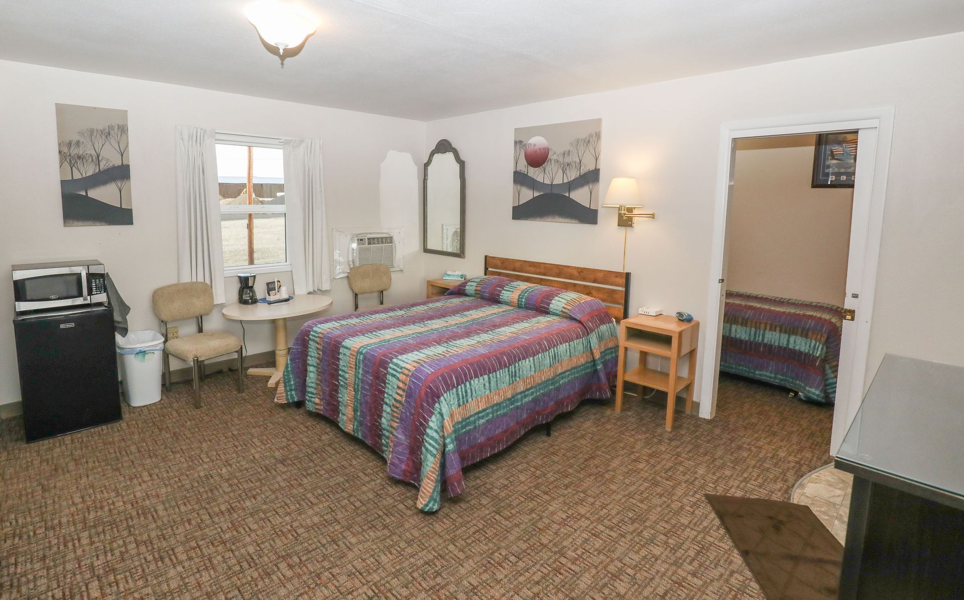 A hotel room with a bed , chairs , table and microwave.
