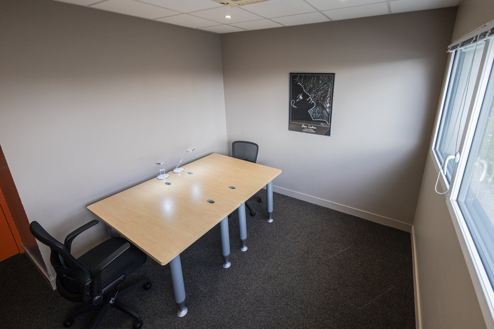 Petit bureau avec un bureau, deux chaises, une fenêtre et des œuvres d'art au mur.