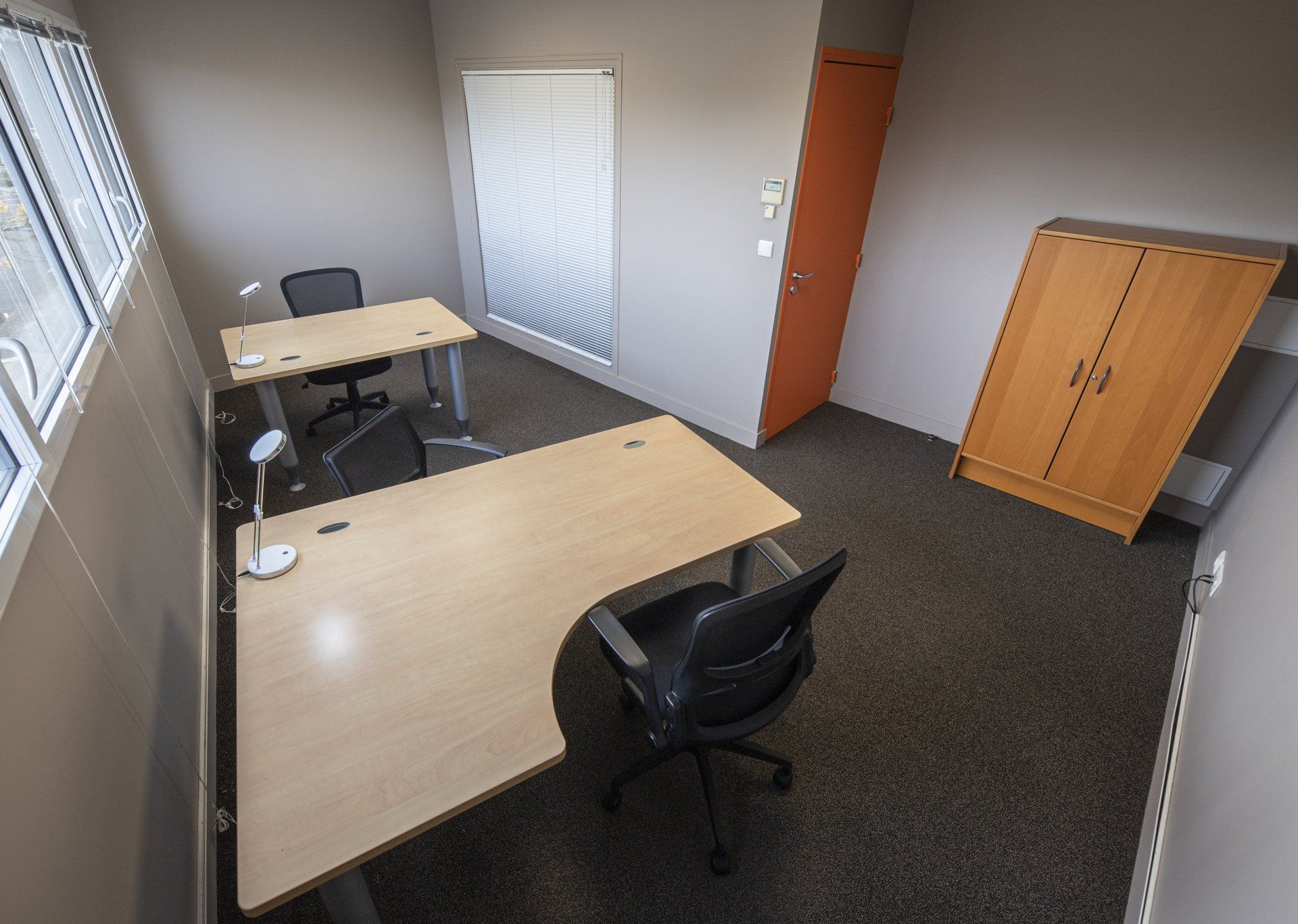 Espace de bureau avec deux bureaux, chaises, fenêtre, porte et armoire.
