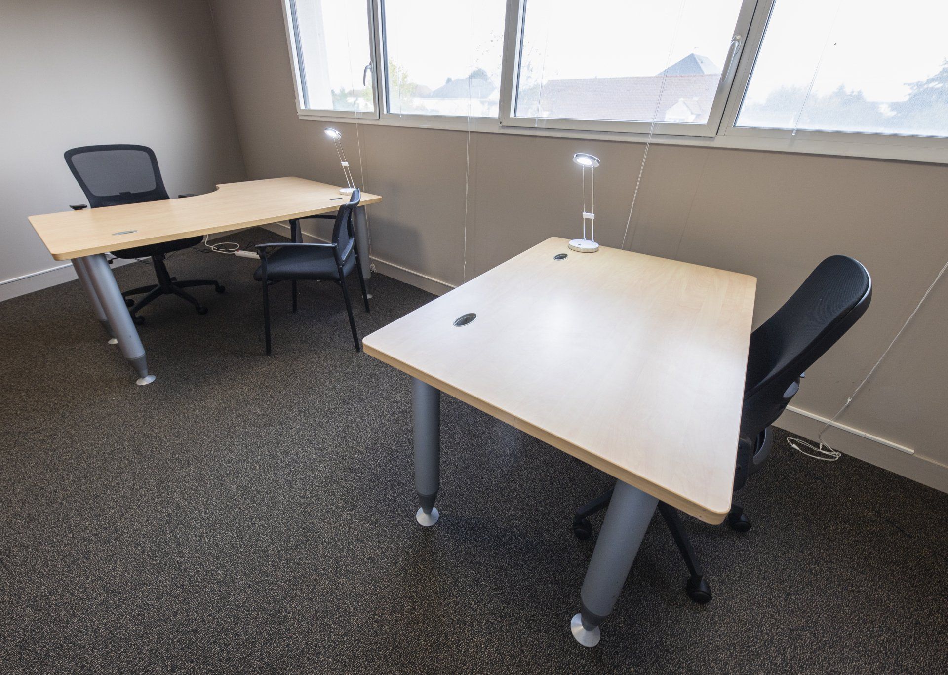 Deux bureaux avec des chaises dans un petit bureau. Fenêtres le long du mur.