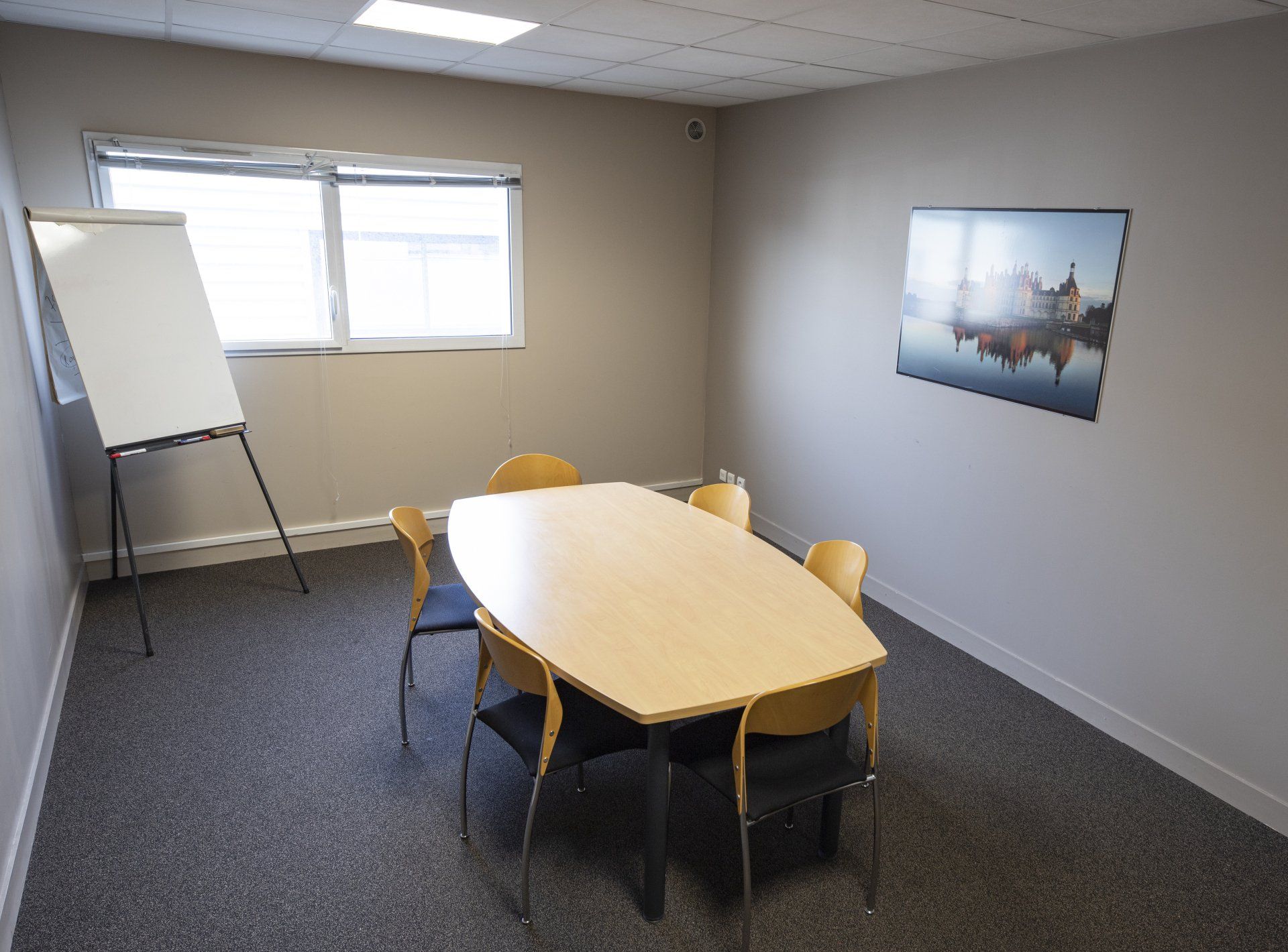 Salle de réunion avec table ovale, chaises, tableau blanc et œuvres d'art ; murs et moquette aux tons neutres.