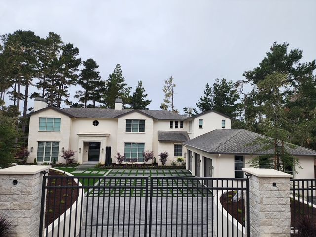 White two-story house with black gate and trees; gray sky.