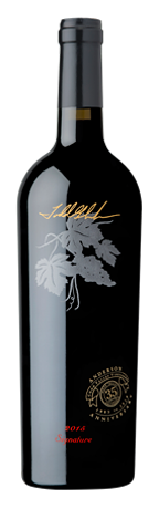 A black wine bottle with a gold signature, a silver grape leaf illustration, and a gold seal on a dark background.