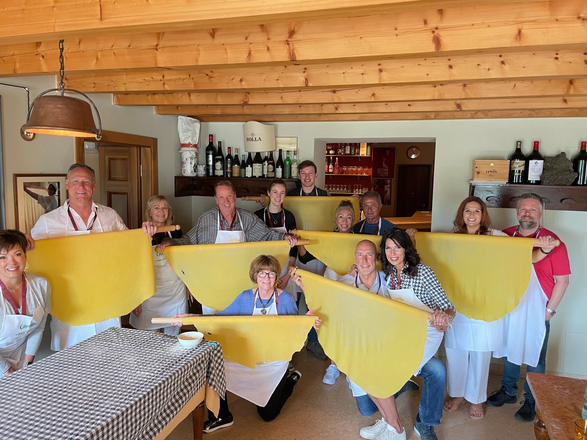 A group holds large sheets of fresh, yellow pasta in a rustic kitchen setting.