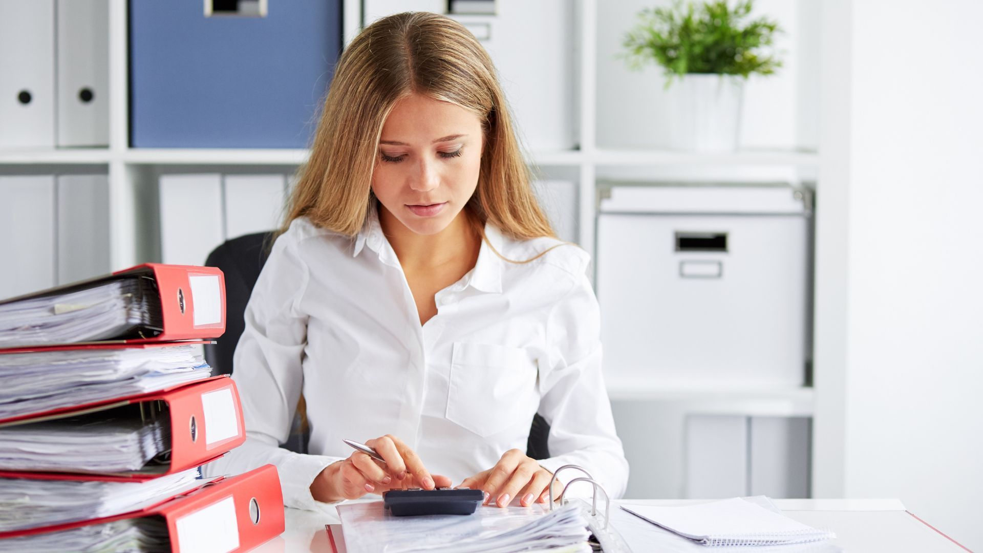 Woman calculating sole trader tax with self-assessment form, receipts and calculator on desk