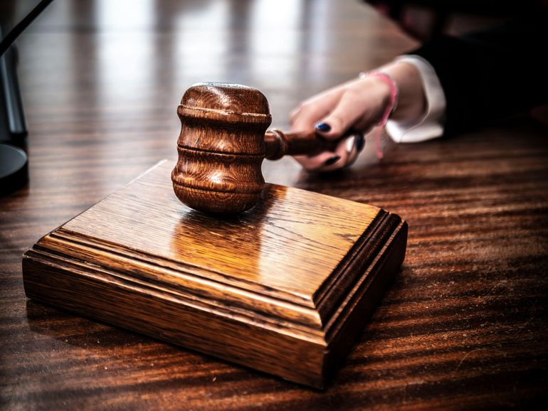 Judge’s gavel on a wooden base, with a hand in the background reaching for it