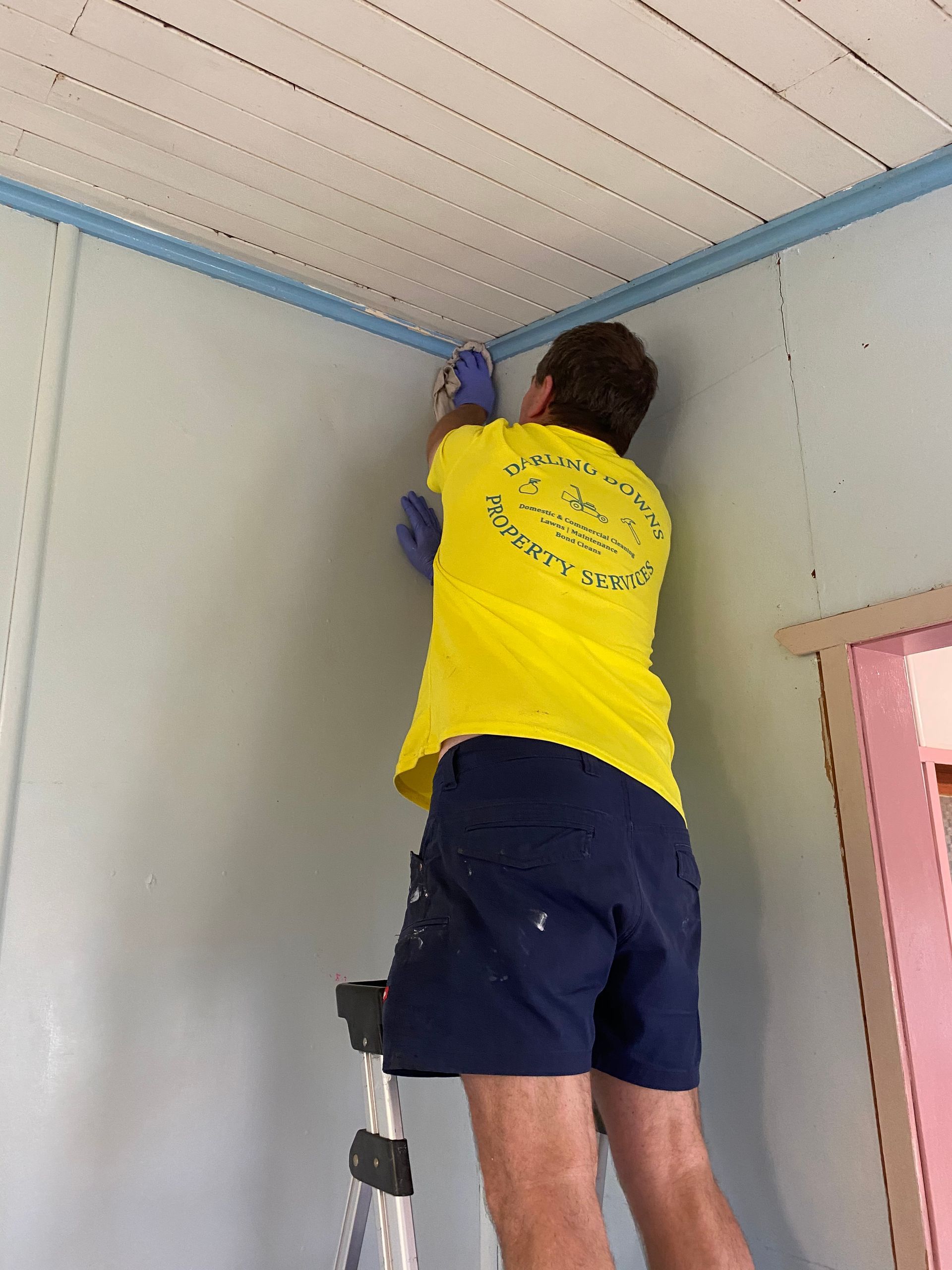 Man in a yellow company shirt cleaning walls - Cleaning Services in Darling Downs, QLD