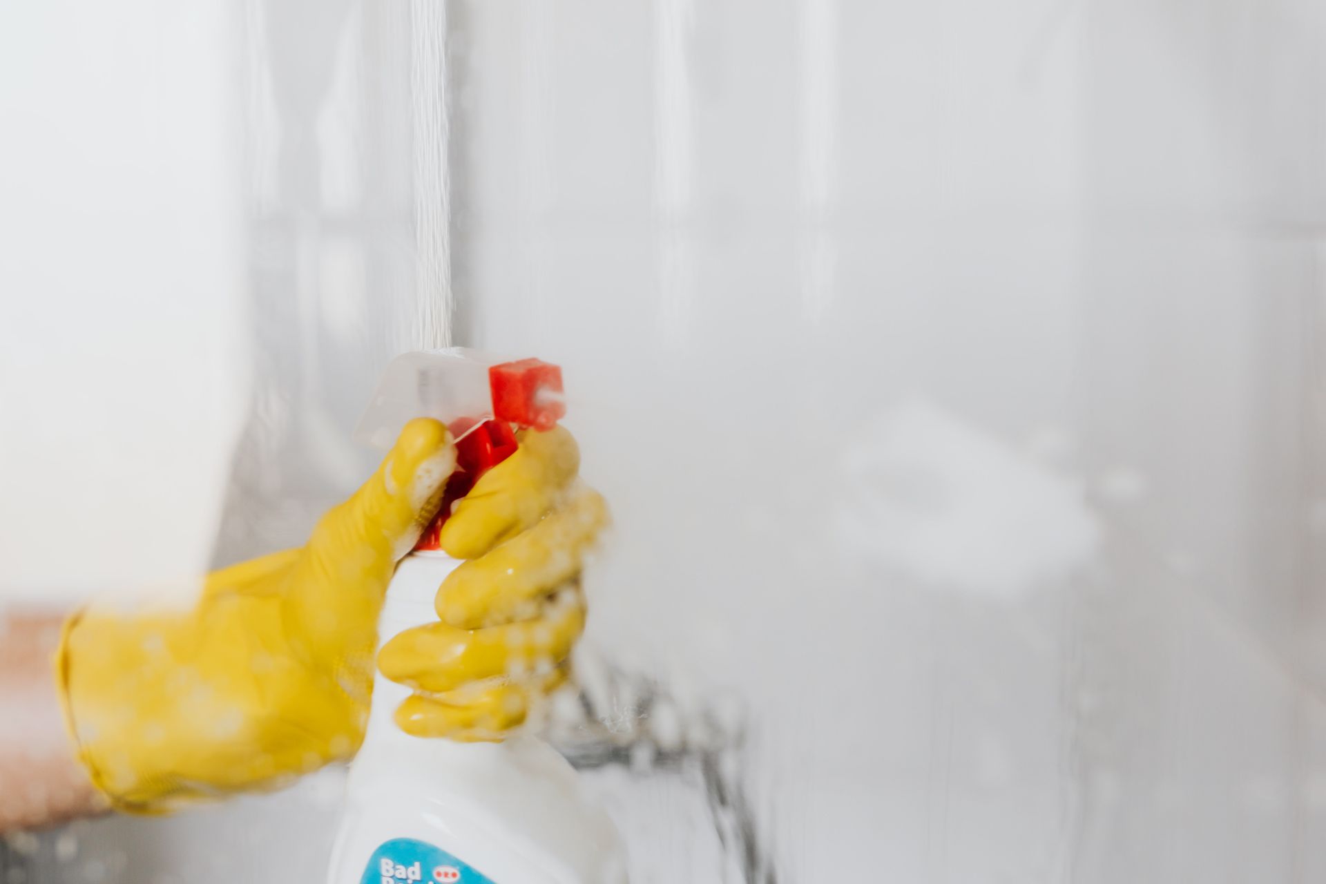 Person with yellow gloves spraying down shower doors - Cleaning Services in Darling Downs, QLD