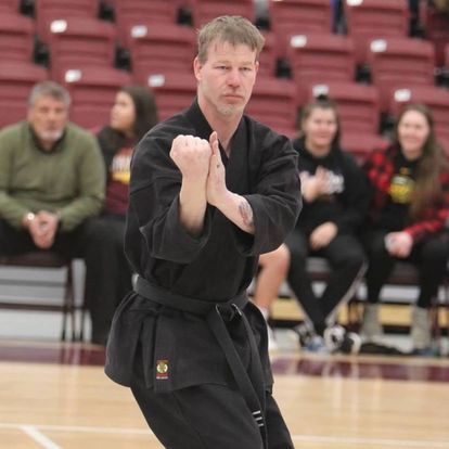 a man in a black karate uniform is standing on a basketball court .