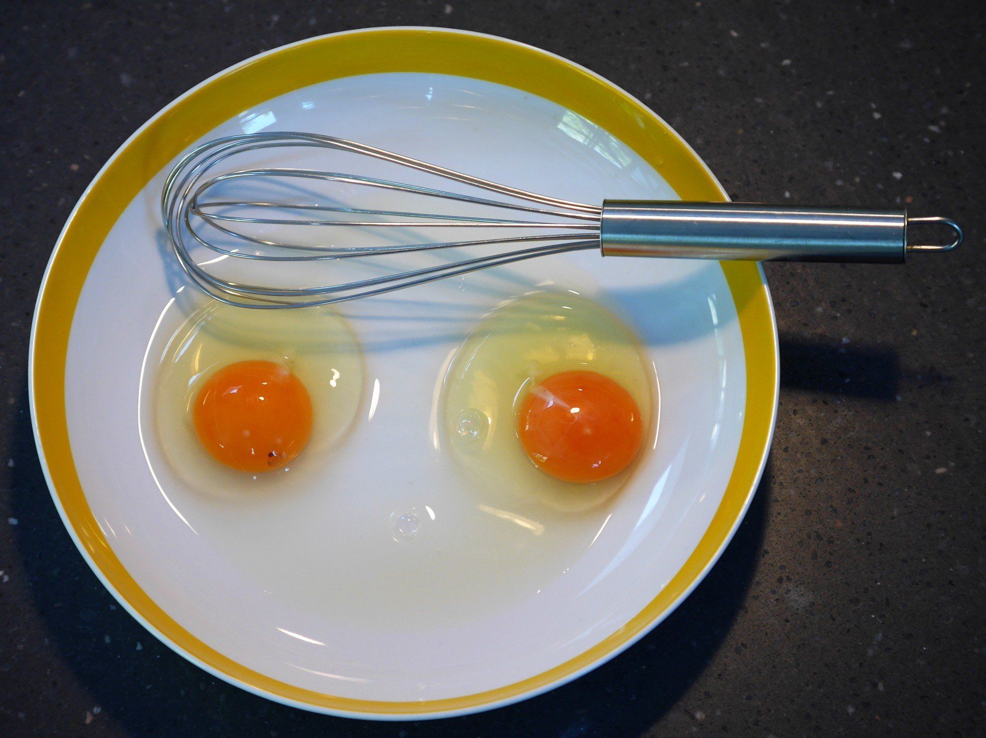 Two egg yolks in a dish with a whisk