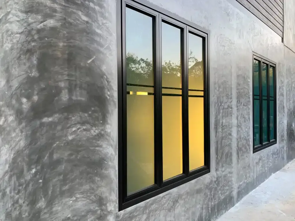 Black-framed windows on a gray concrete wall reflect a golden sunset.