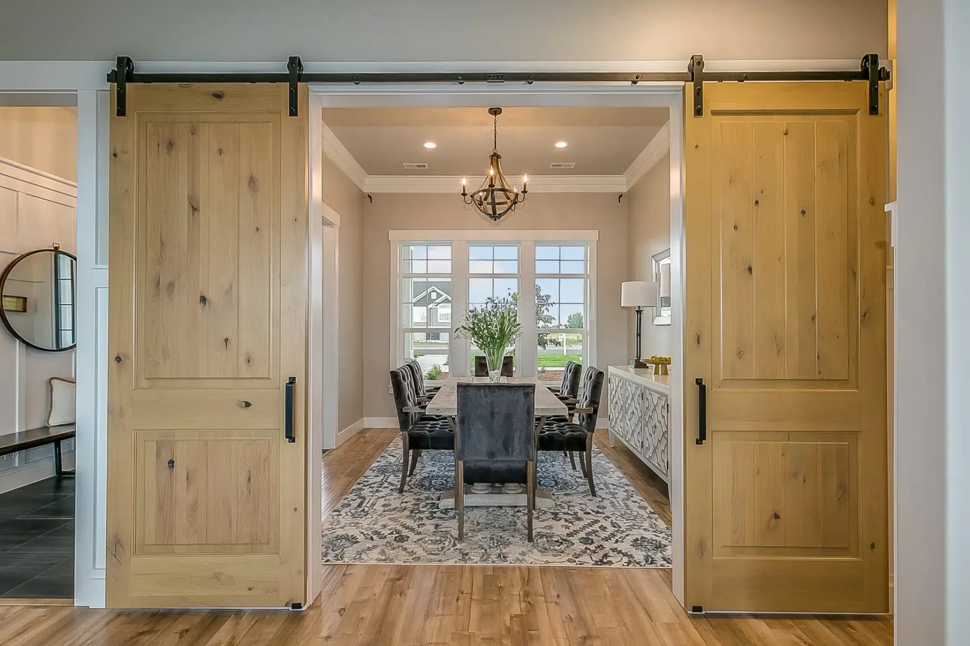 Wooden barn doors open to a dining room with a table, chairs, and chandelier.