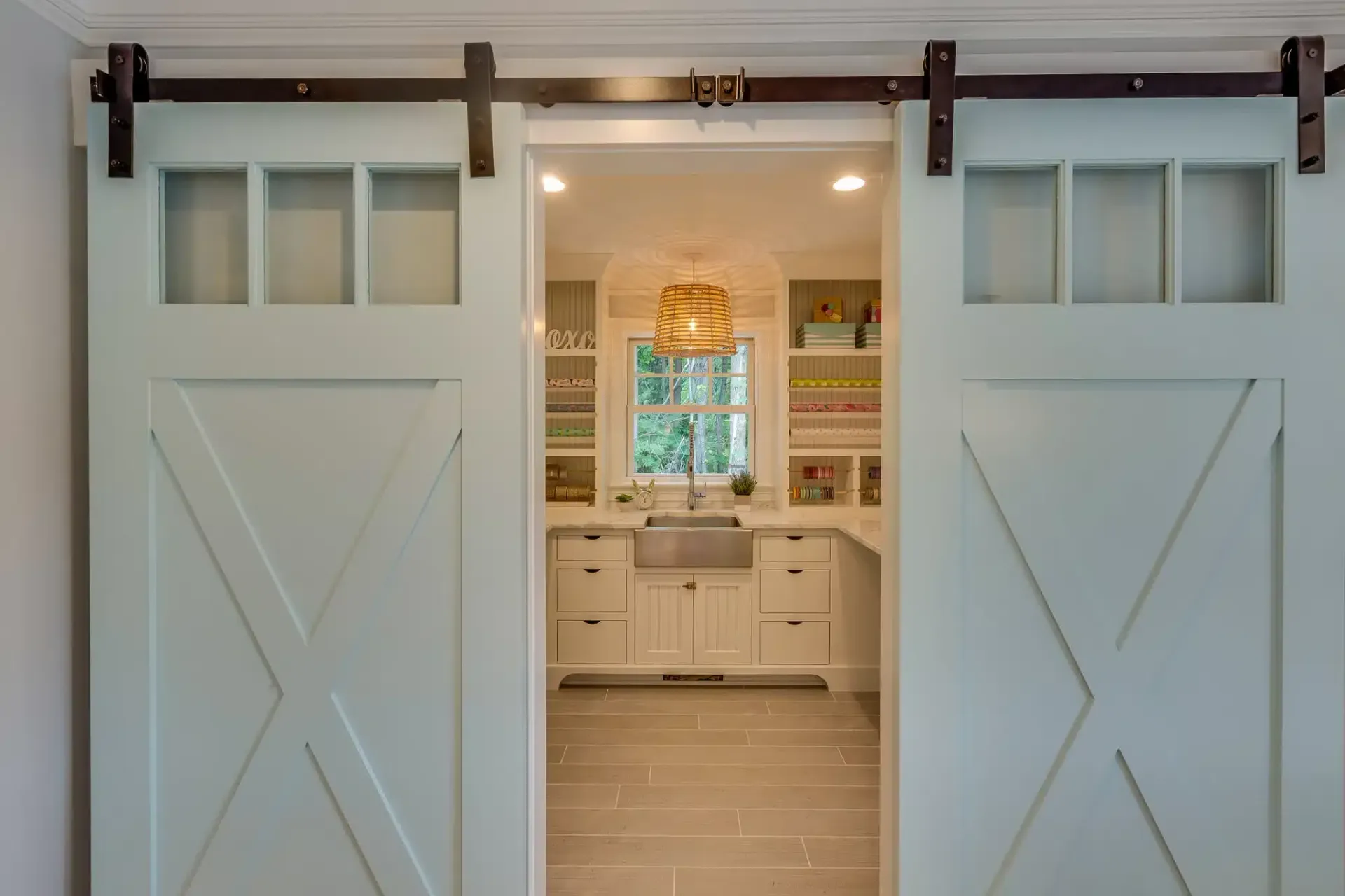 Light blue sliding barn doors open to reveal a bright, white kitchen with a window and a large sink.