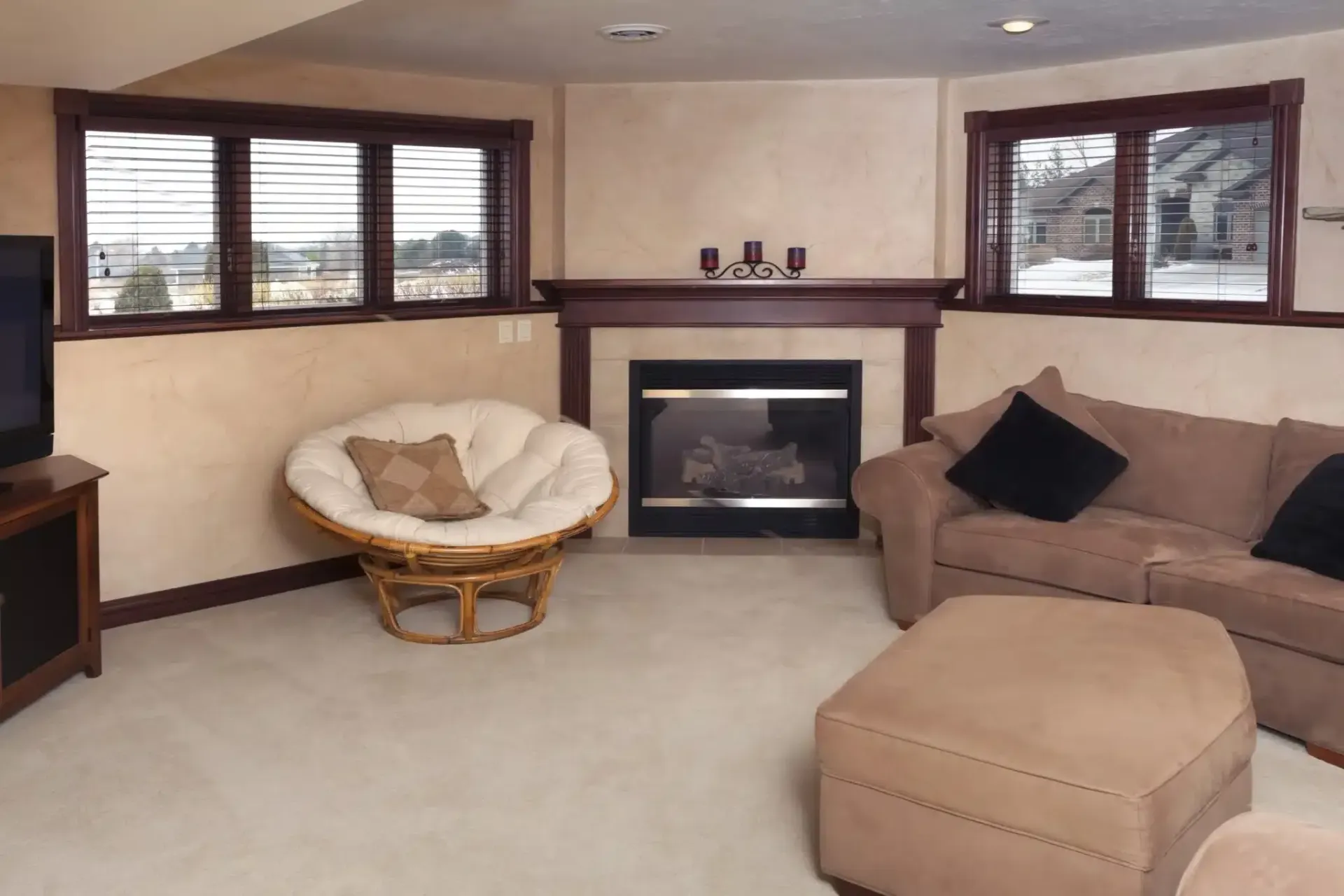 Living room with fireplace, beige walls, windows, papasan chair, sofa, and ottoman.