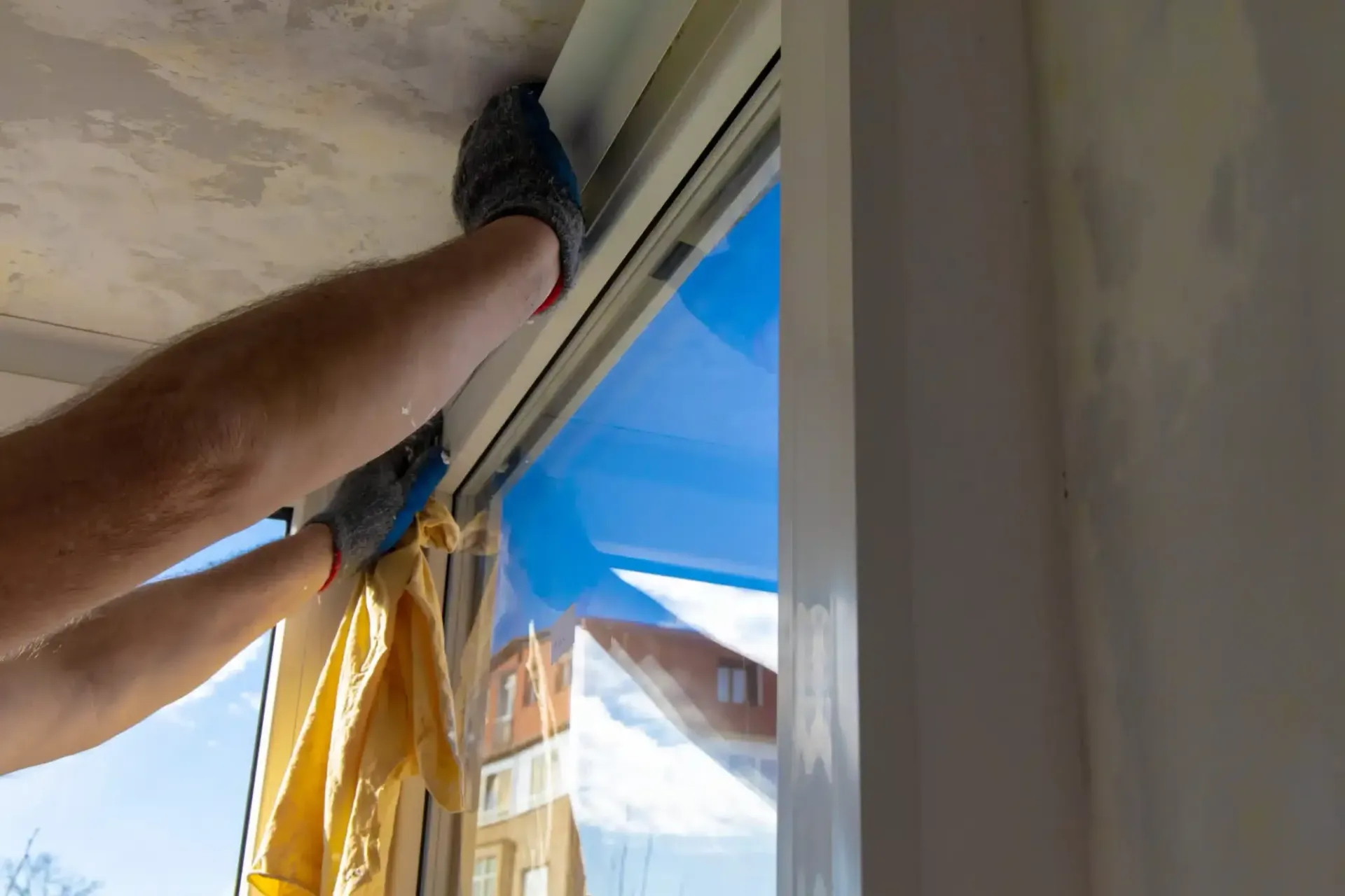 Person wearing gloves installing window covering.