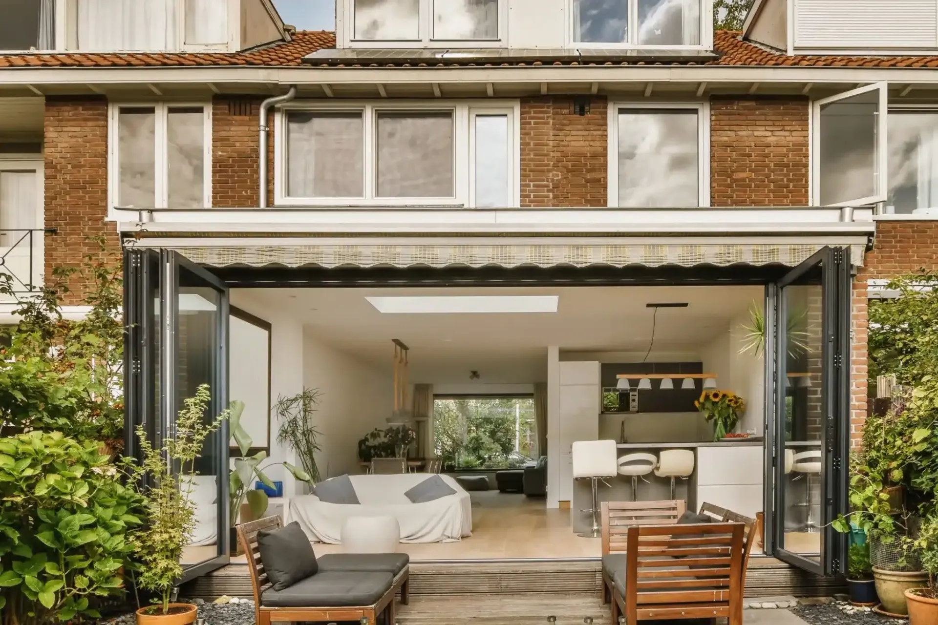 Exterior view of a home with open doors leading to a modern interior, featuring outdoor seating.