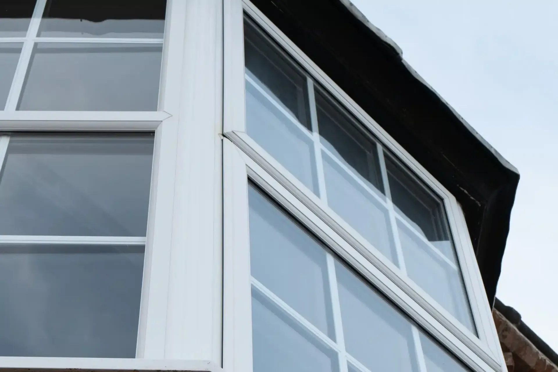White-framed bay windows on a building with a dark roof against a blue sky.