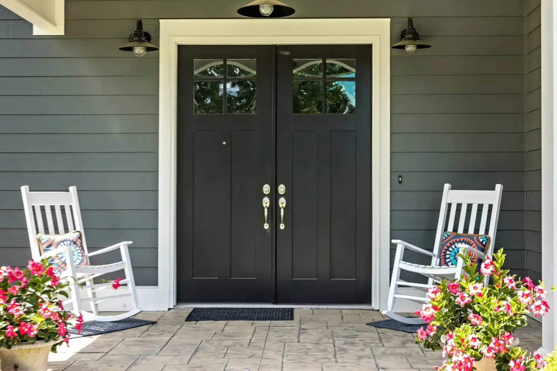 Exterior of a house with gray siding, black double doors, white trim, and two rocking chairs.
