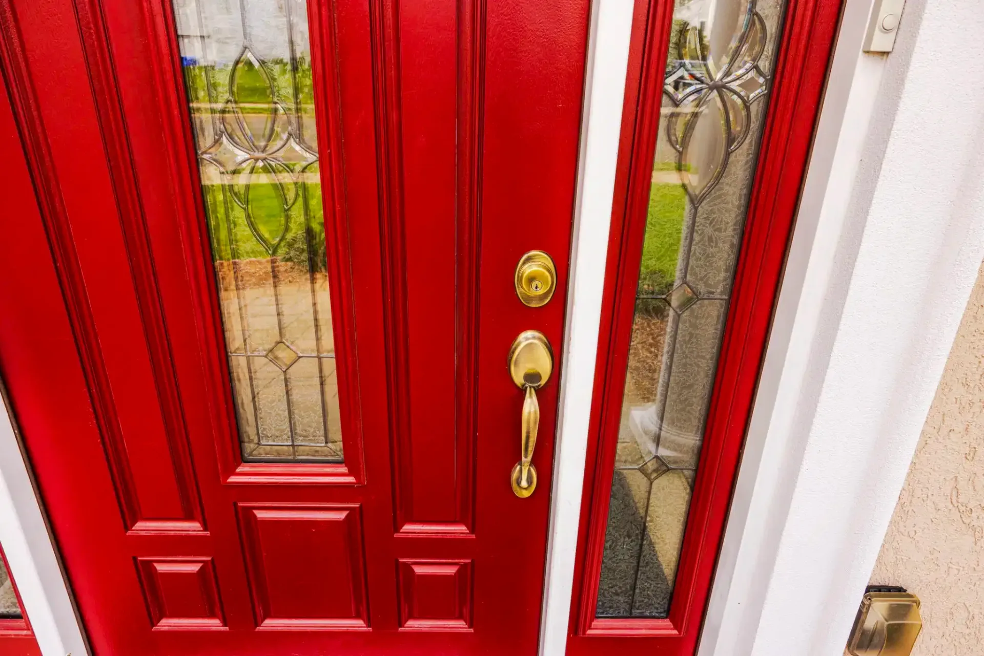 Red front door with gold hardware and glass side panels.
