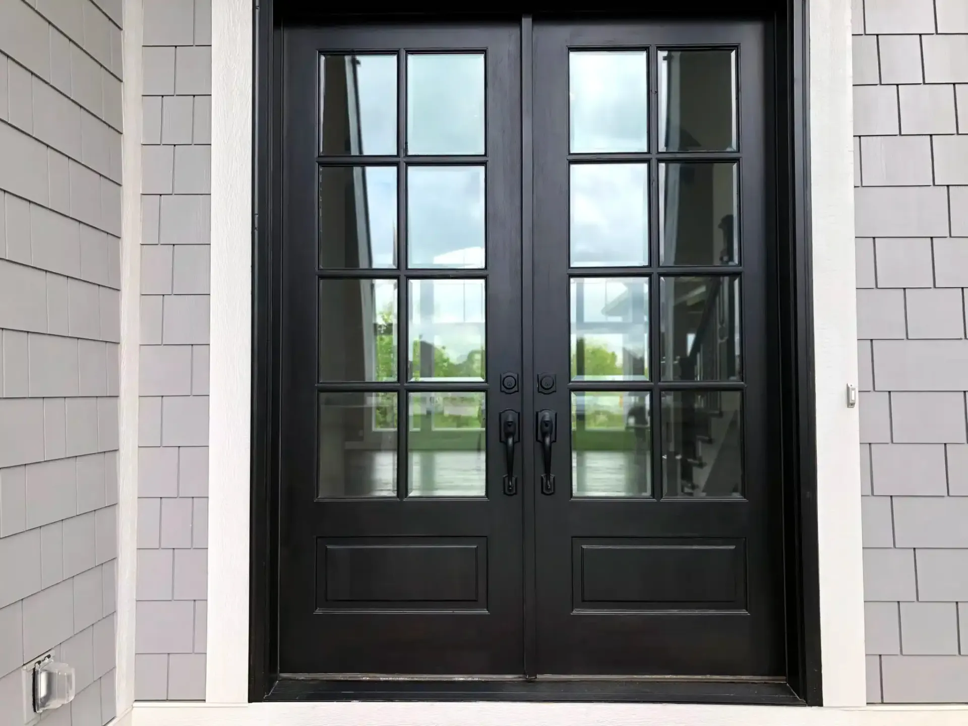Black double front doors with glass panes, framed by gray siding and white trim.