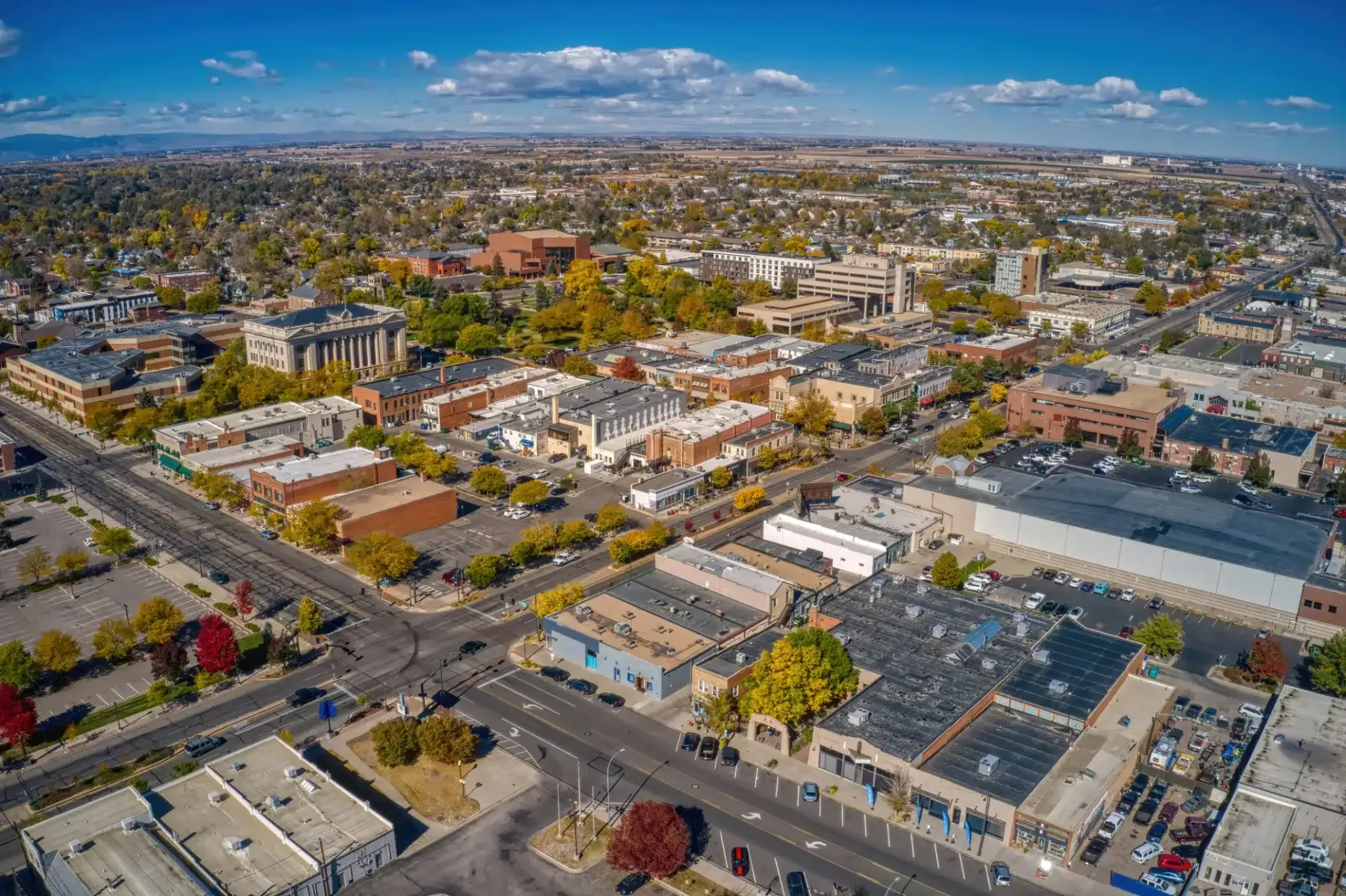 Aerial view of a city with buildings, roads, and trees under a blue sky with clouds.