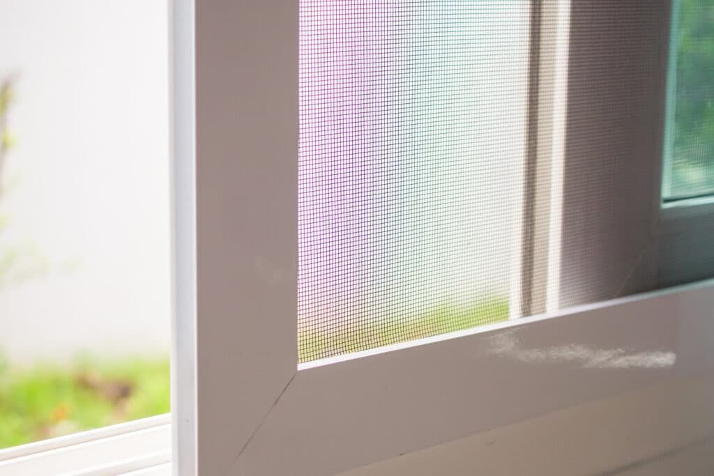 Close-up of a white window frame with a screen and a view of green grass.