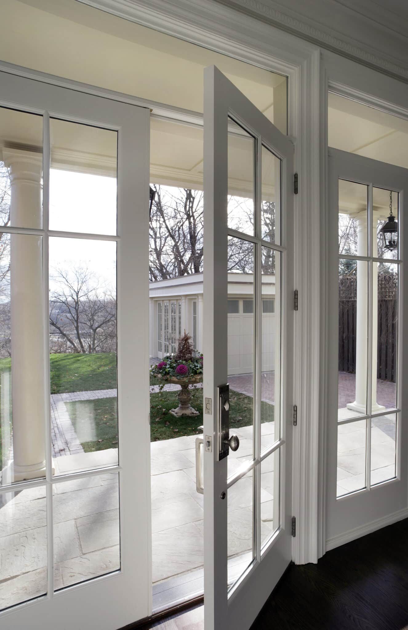 White French doors open onto a patio. Sunlight illuminates the outdoor space with a distant building.