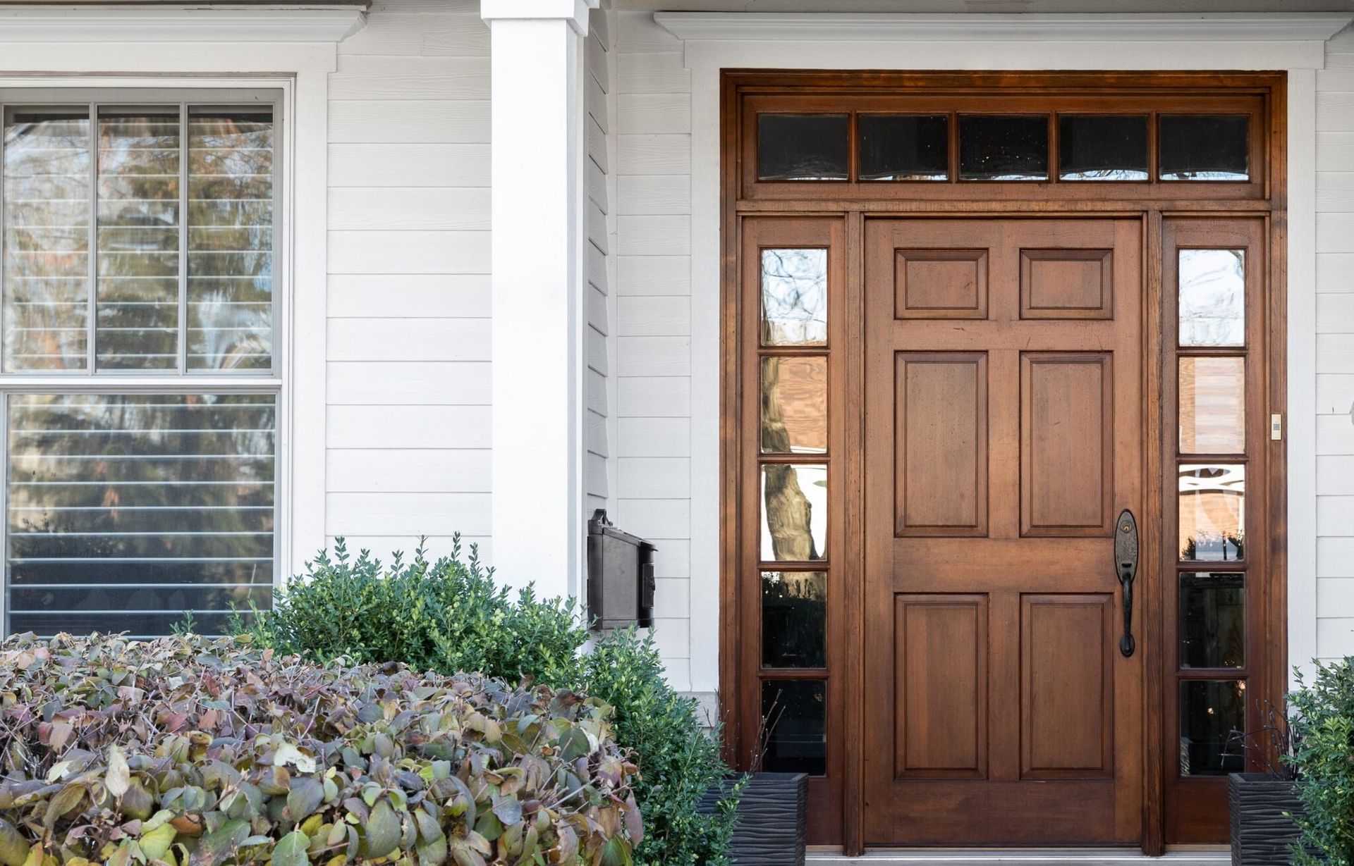 White house entrance with wooden door, sidelights, transom, and window.