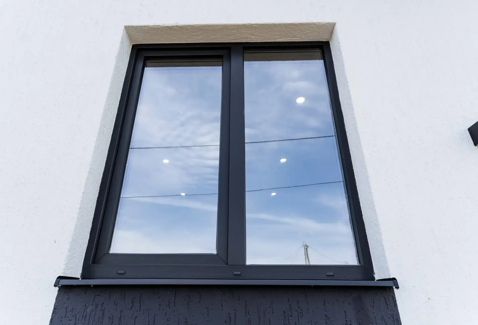 Black-framed window on a white building, reflecting a cloudy sky.