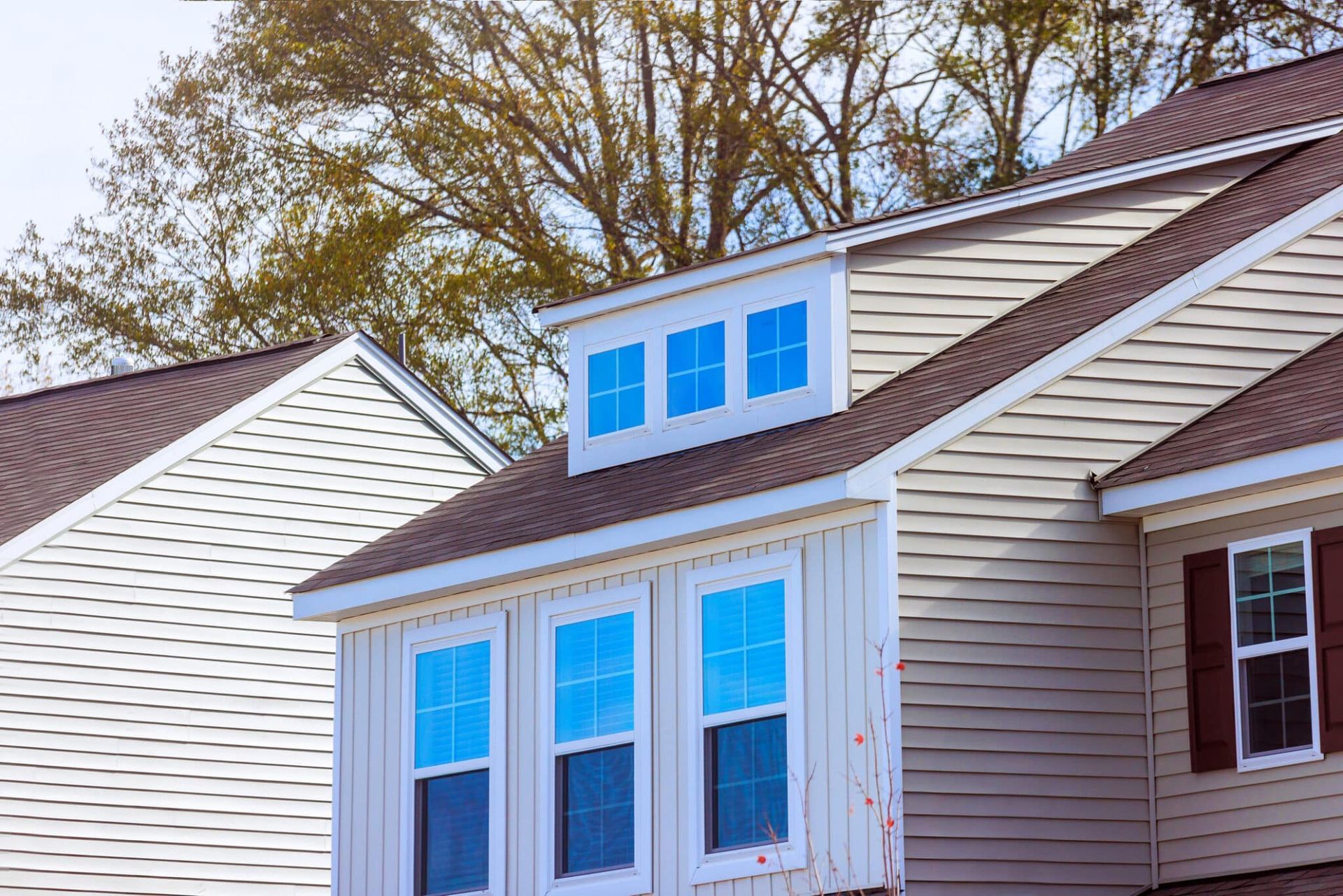 Beige house exterior with windows, brown roof, and trees in the background.