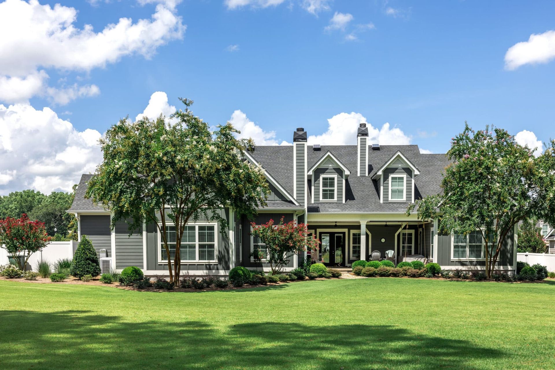 Gray house with green lawn, trees, and blue sky.