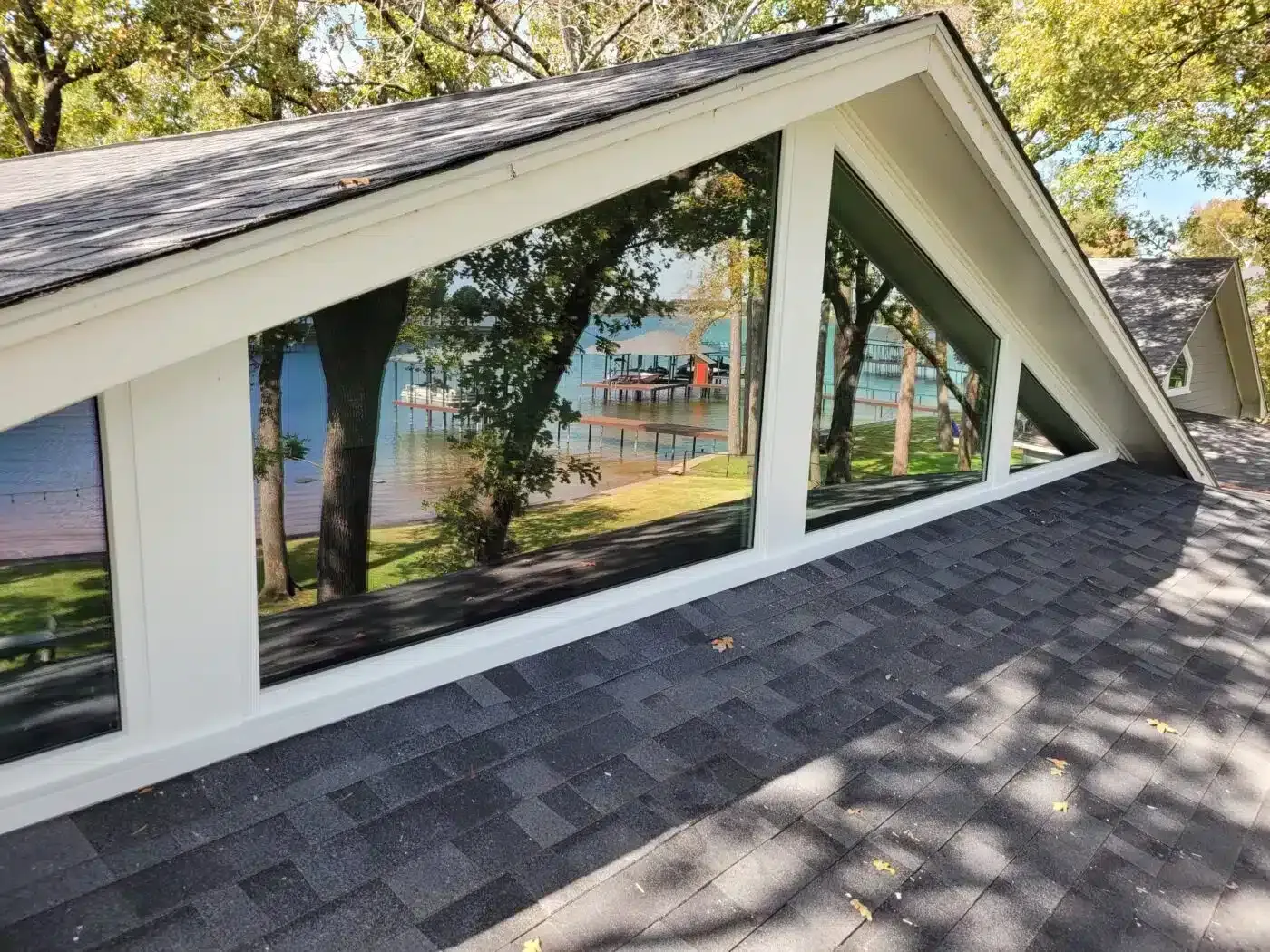 Triangular windows in a roof show a lake scene with docks, trees, and blue water. White trim, gray roof shingles.