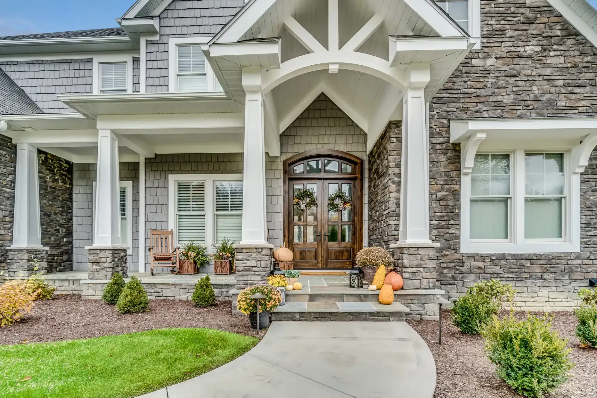 Gray stone house with arched doorway, white columns, and pathway leading to the entrance.