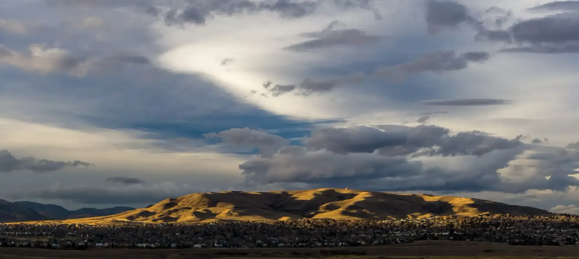 Dramatic cloudy sky over a dark, silhouetted landscape with a hint of sunlight.