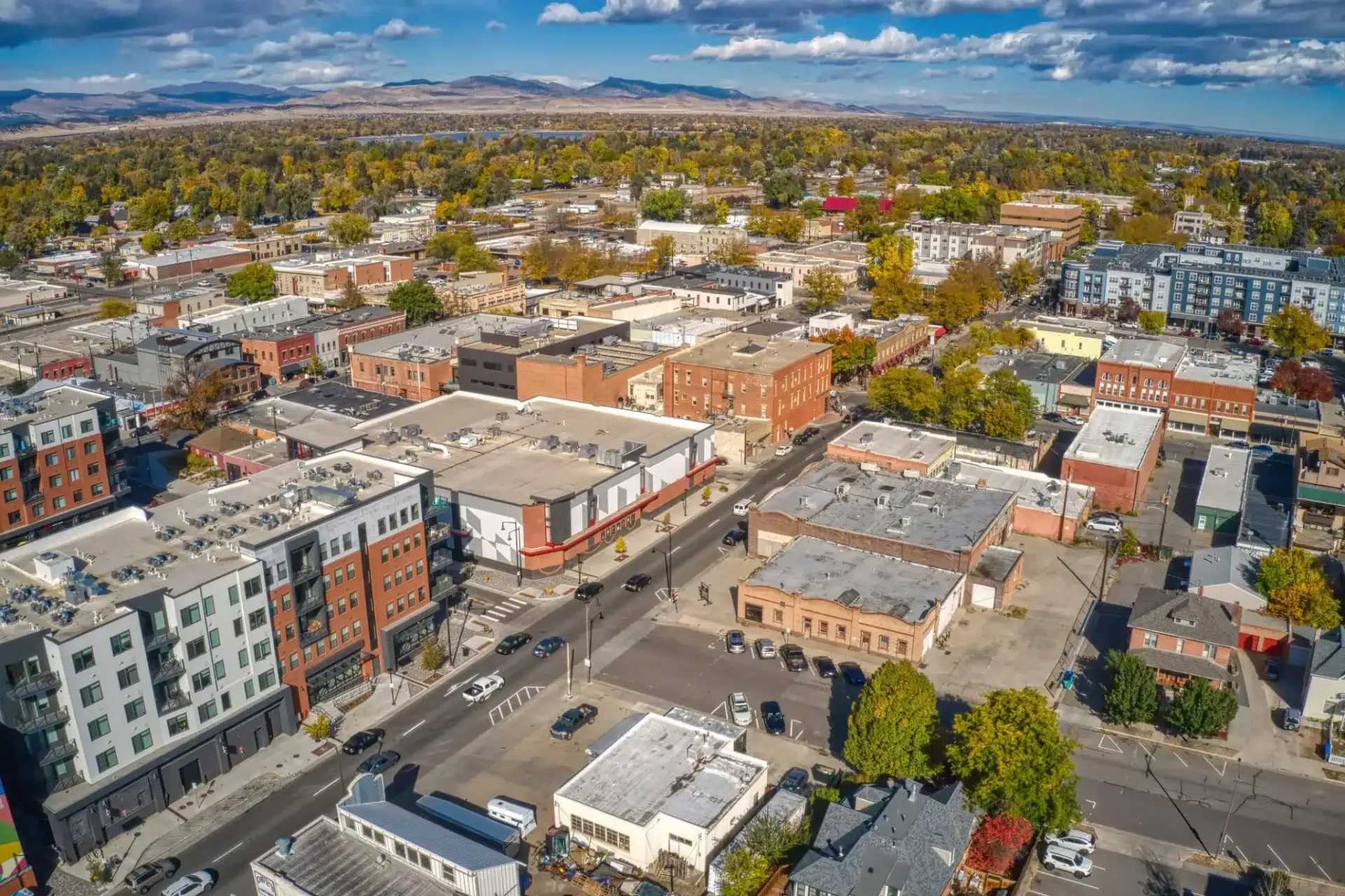 Aerial view of a town with commercial buildings, streets, and trees under a blue sky.