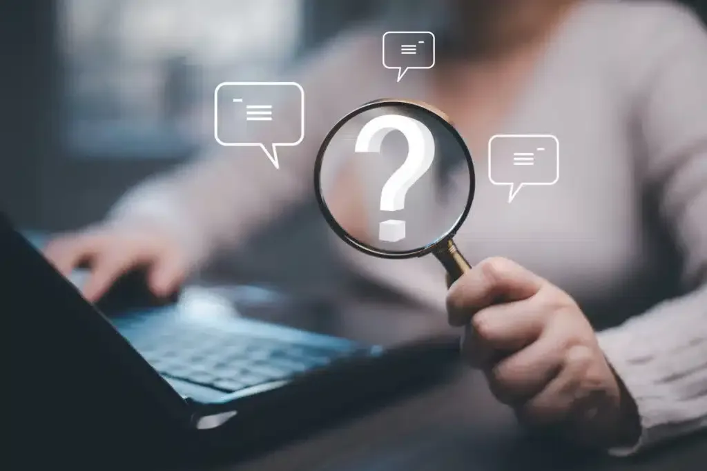 Woman using laptop, holding magnifying glass over a question mark icon with message bubbles.