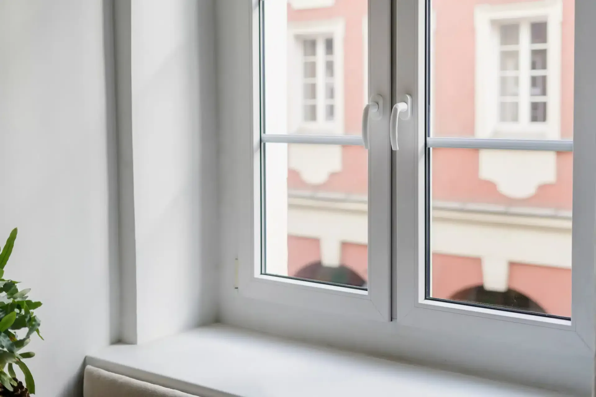 White window with a view of a pink building, inside a white room, daytime.