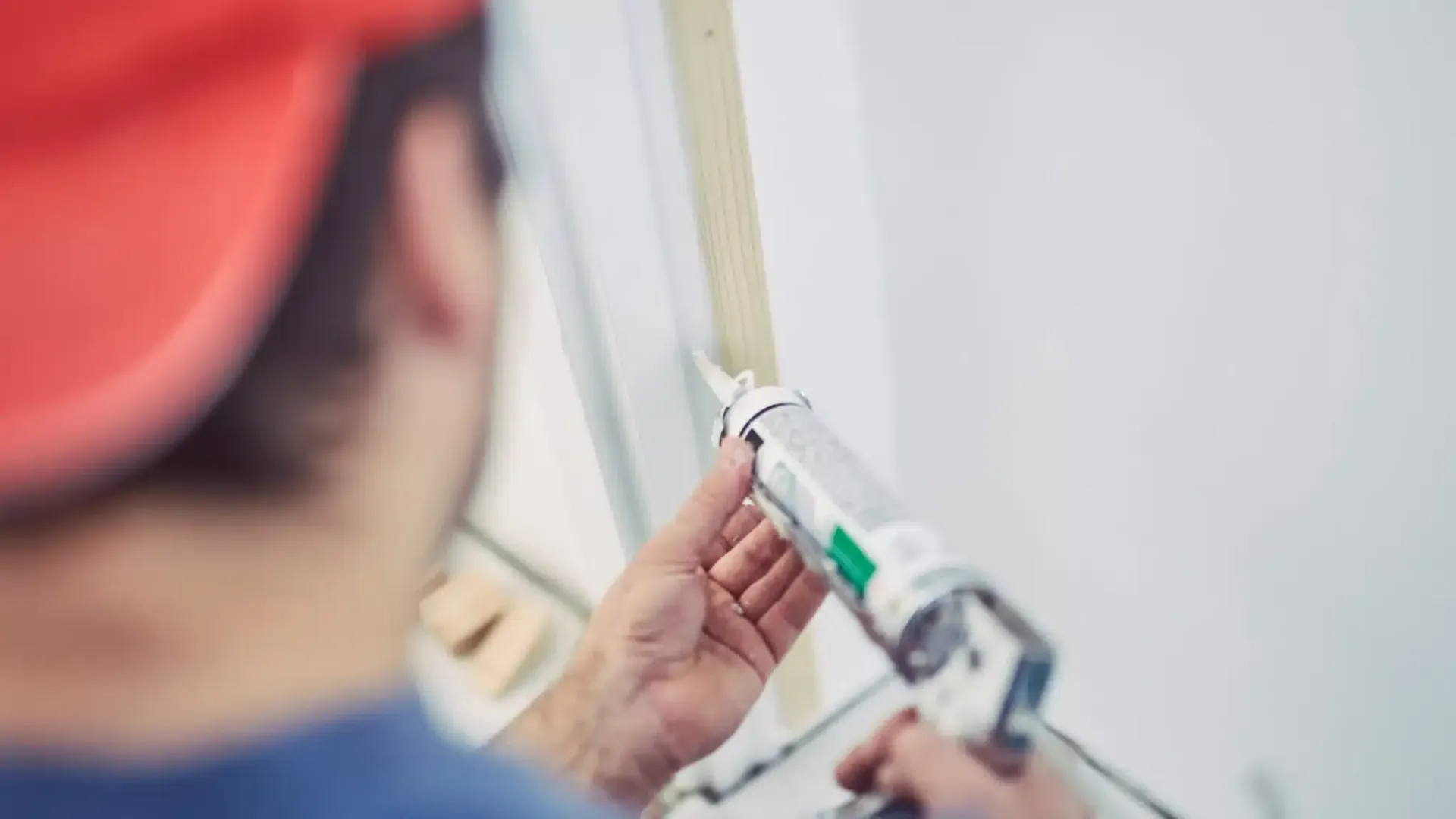 Person applying caulk to a window frame, holding a caulk gun.