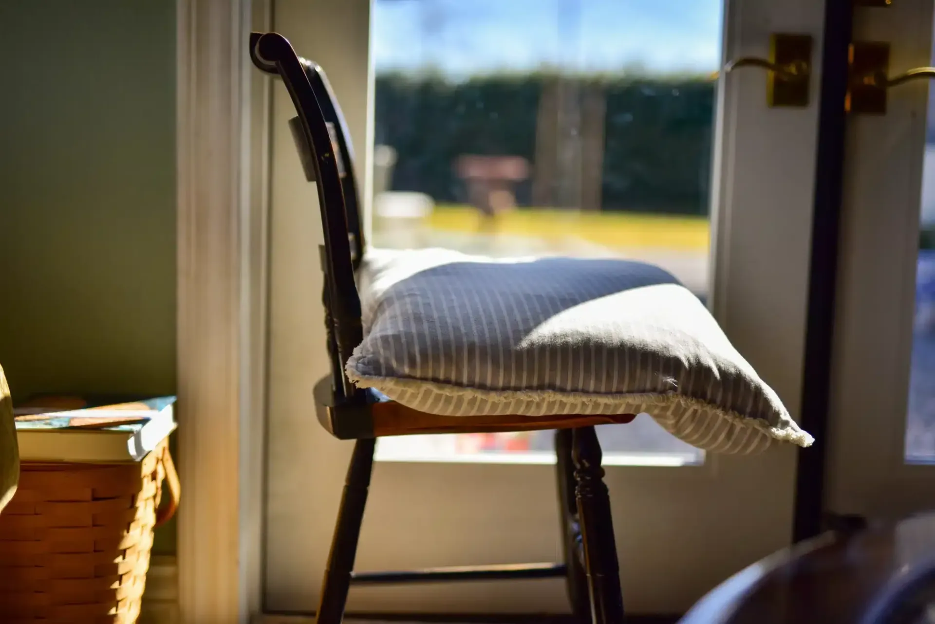 Wooden chair with striped pillow near a bright window.