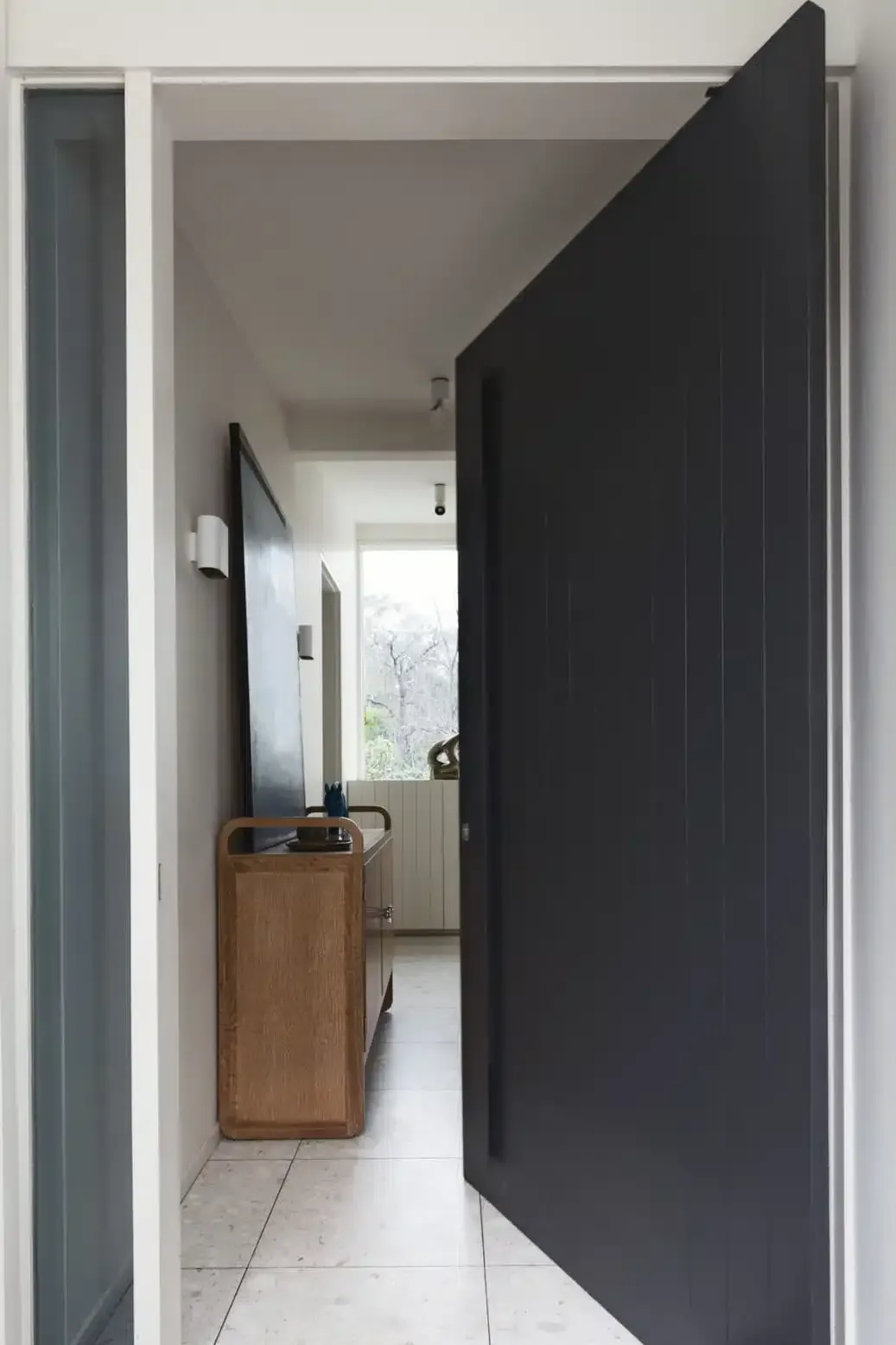 Black front door, partially open to reveal hallway with a wooden console table. White trim.
