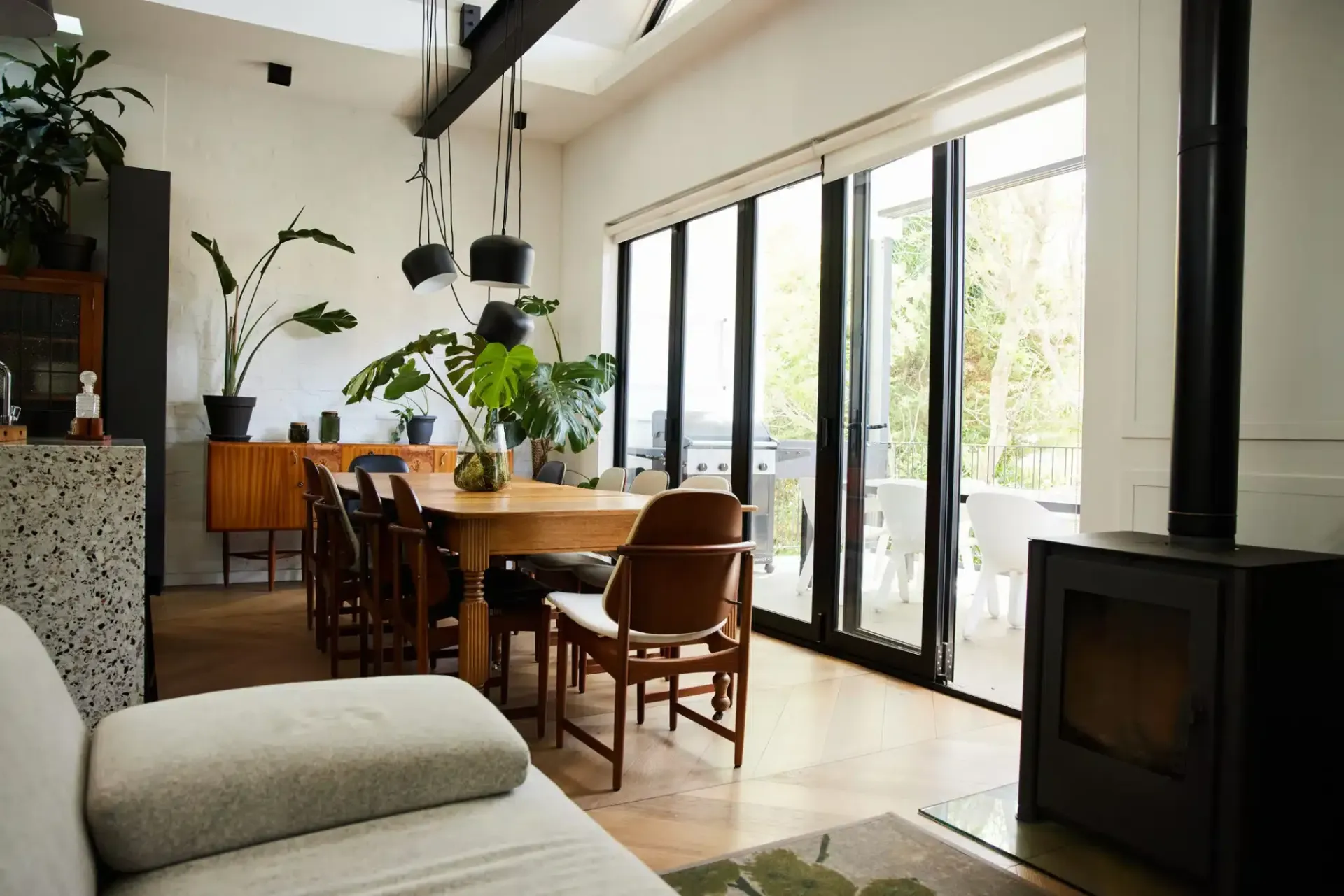 Bright, modern dining room with wooden table and chairs, large windows, plants, and a fireplace.