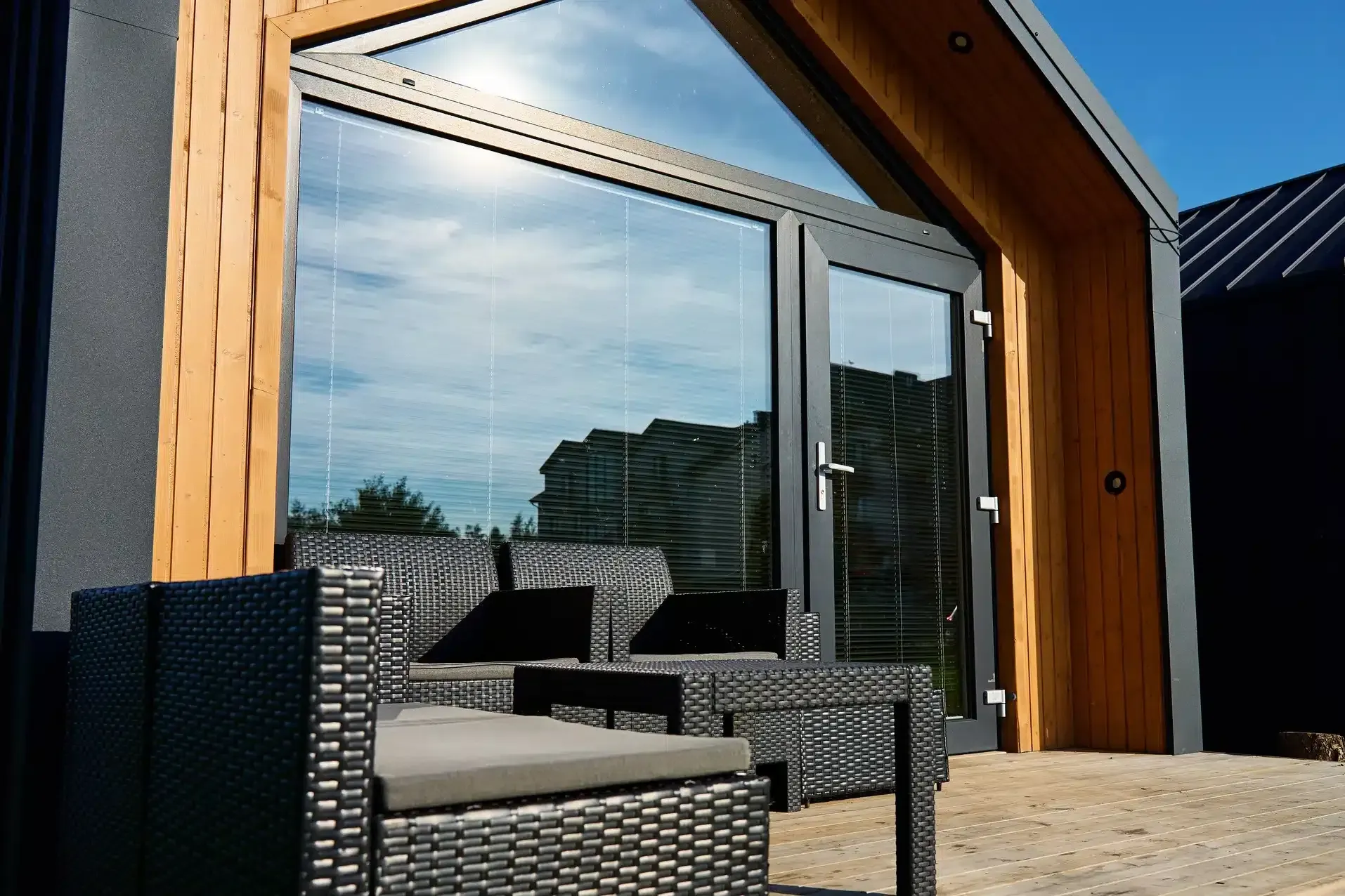 Outdoor seating in front of a modern building with large windows, reflecting the sky and surrounding buildings.