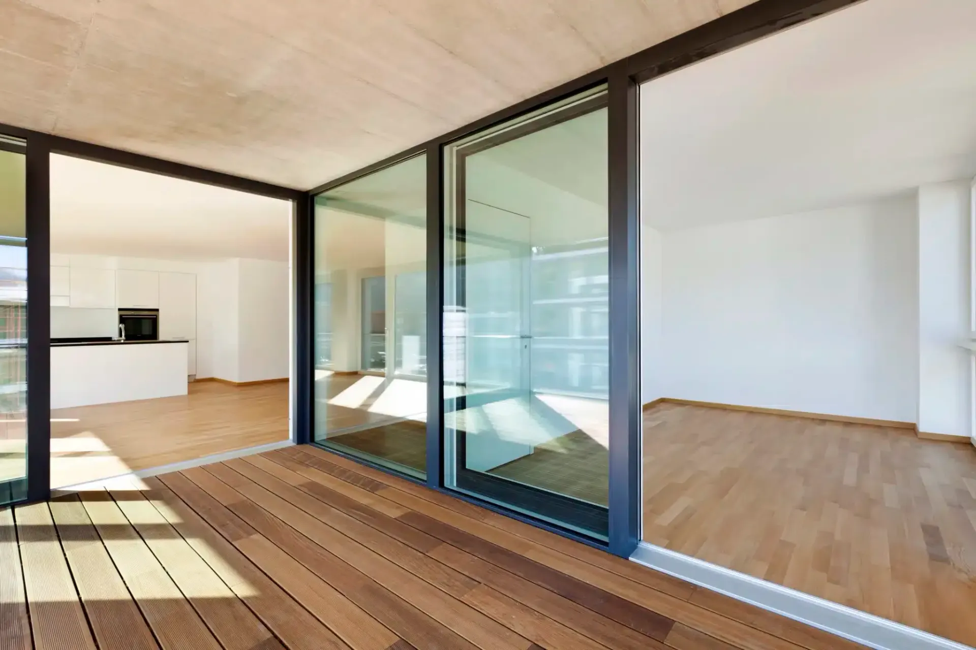 Wooden deck with sliding glass doors opening to a modern interior with wood floors and white walls.