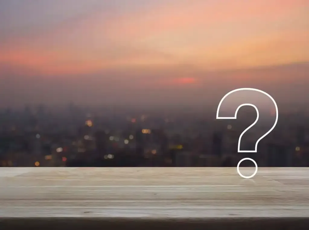 Question mark graphic on wooden surface, city skyline backdrop at dusk.