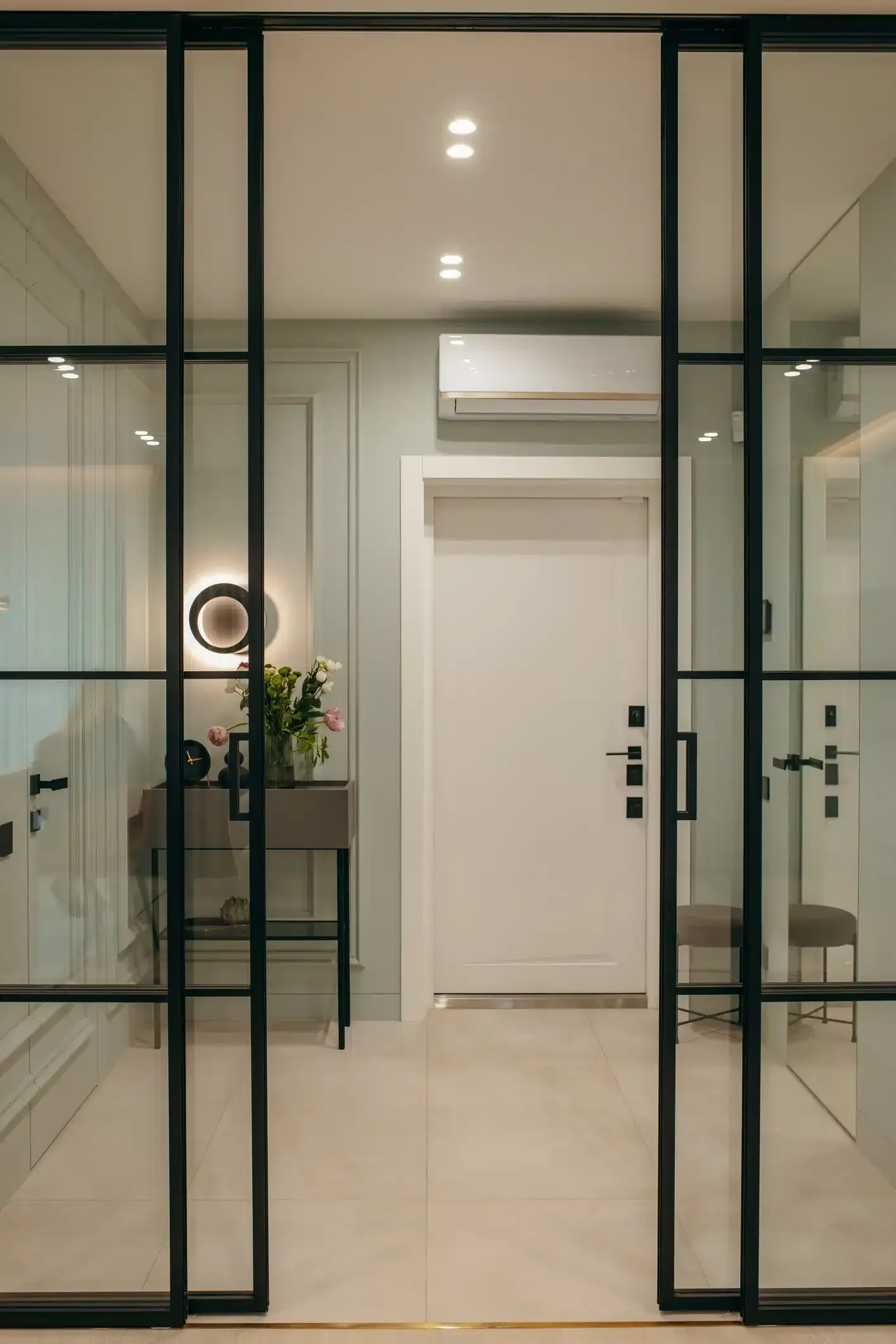 Glass doors with black frames open to a hallway. Light green walls, white door, and tiled floor.