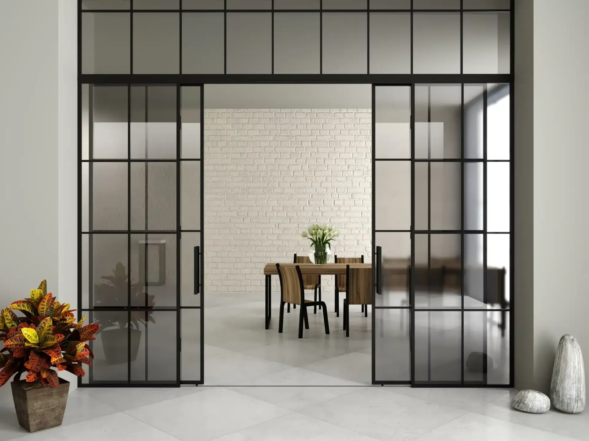 Open glass doors with black metal framing reveal a dining room with a table, chairs, and brick wall.