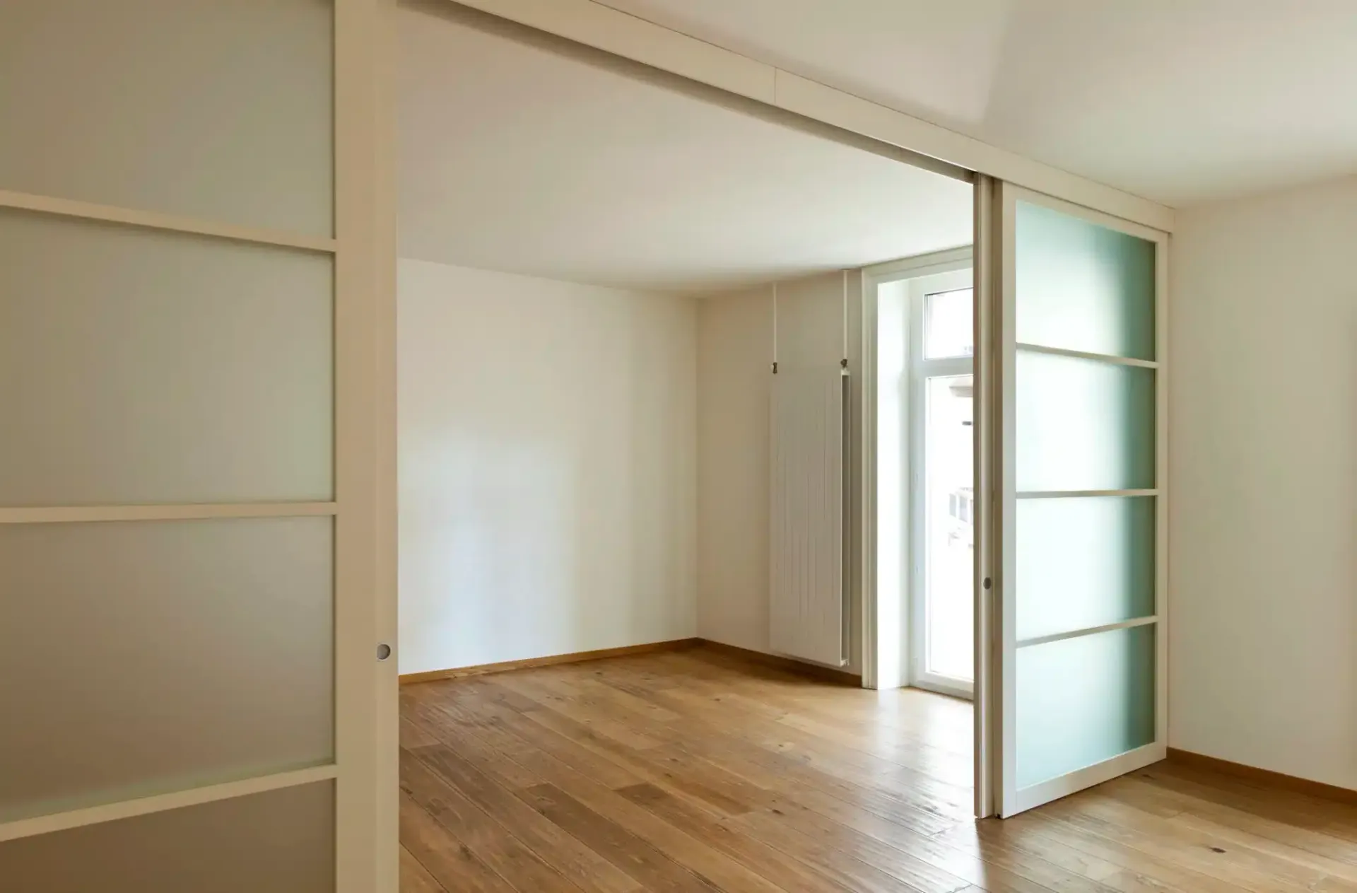 Empty room with sliding frosted glass doors, wooden floors, and white walls.