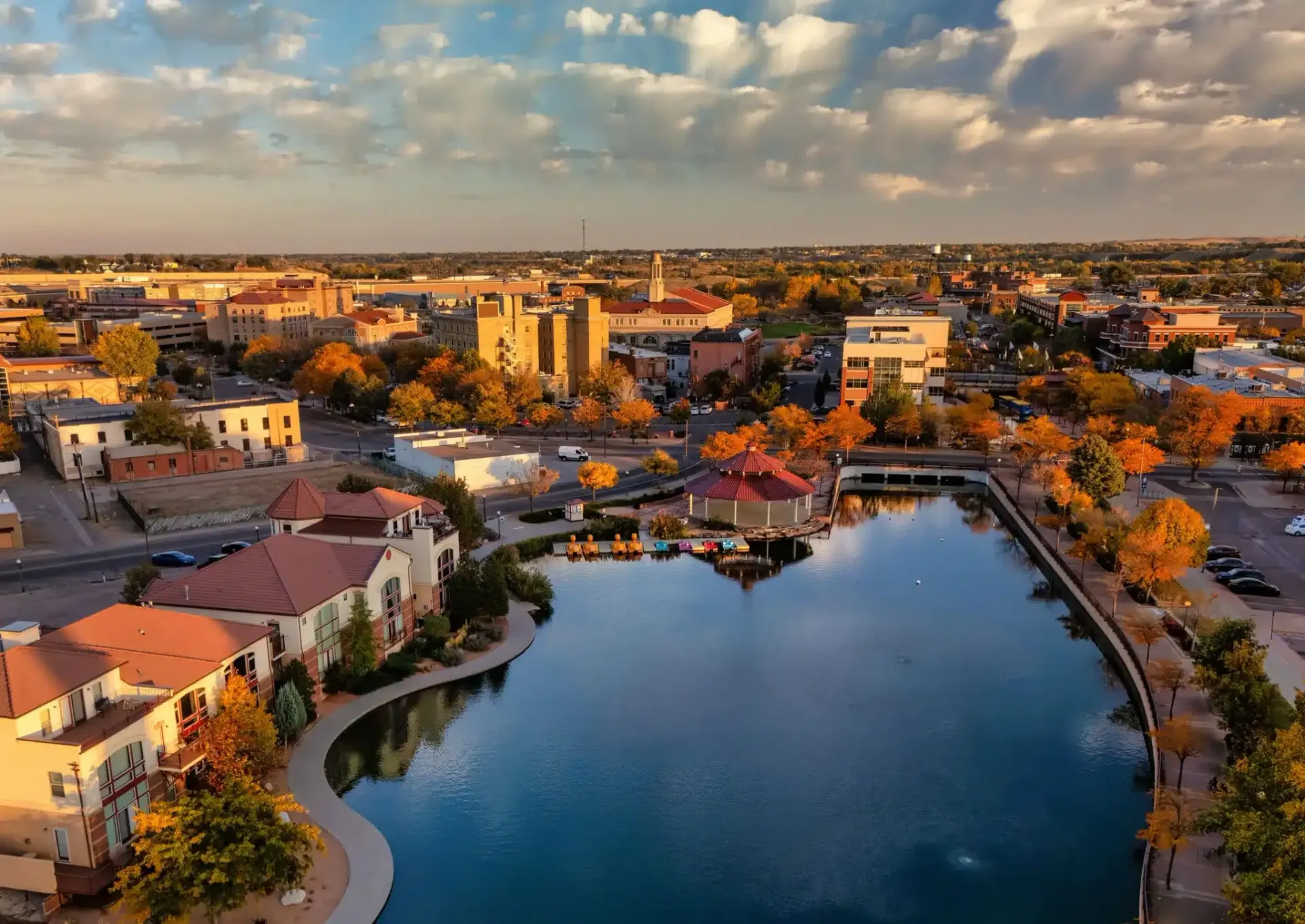 Aerial view of a city with buildings and a lake reflecting the sky at sunset.