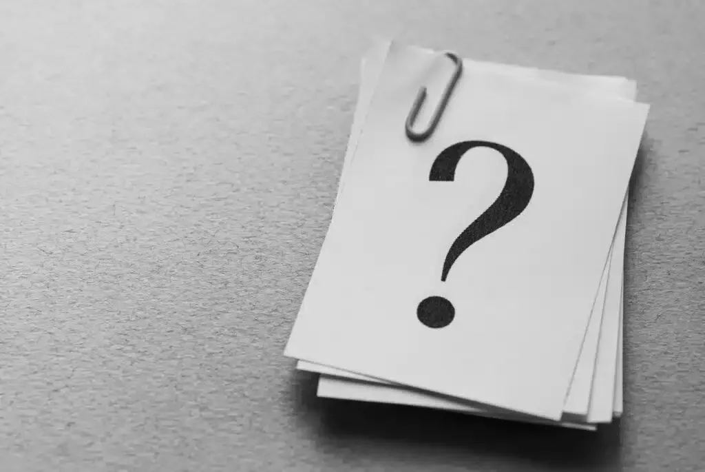 Stack of white notepaper held together by a paperclip, a large question mark on the top sheet.